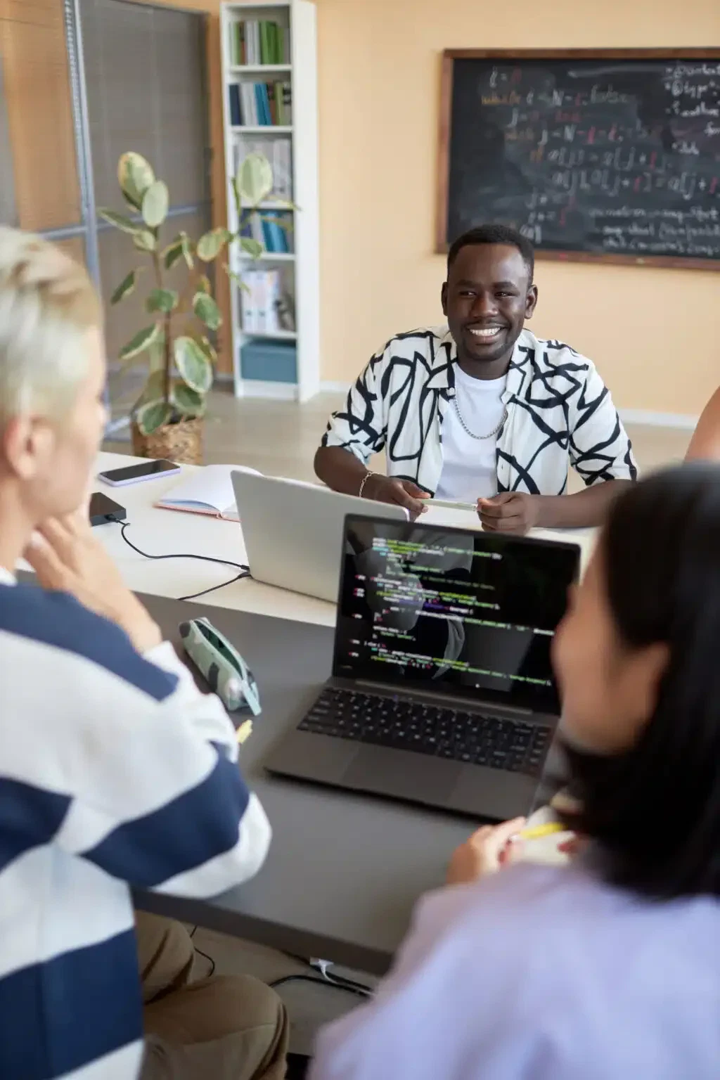 Young cheerful African American man having discussion with two classmates sitting in front of him and decoding data on laptop screen