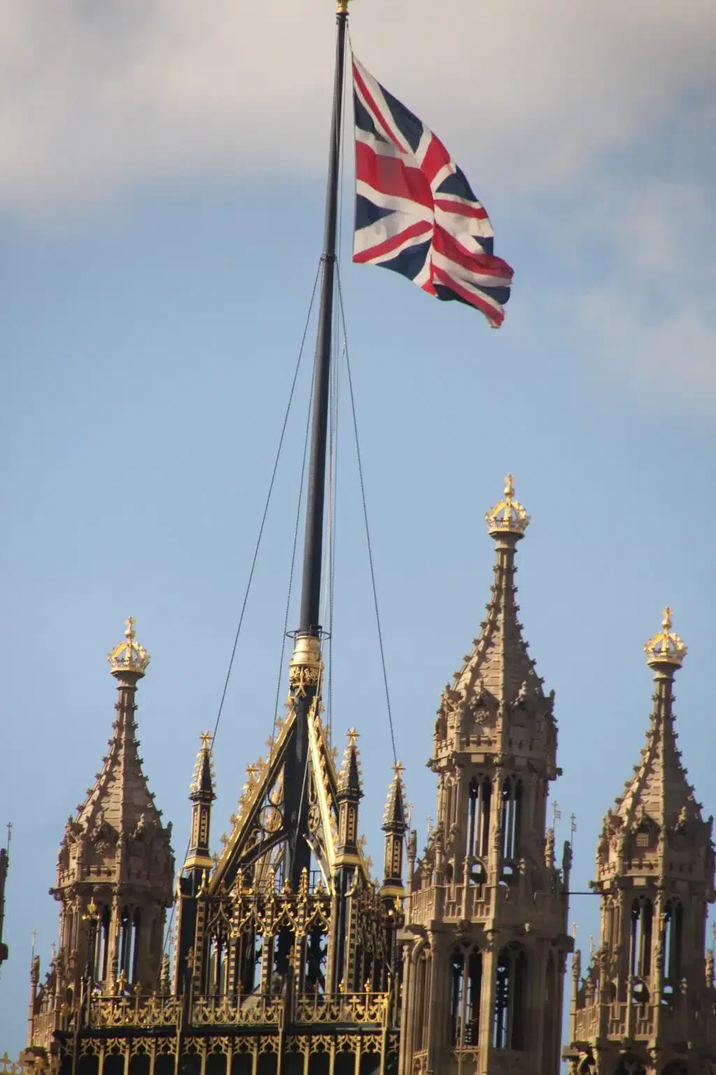 Union Jack flag flying atop the iconic Palace of Westminster in London against a clear blue sky.